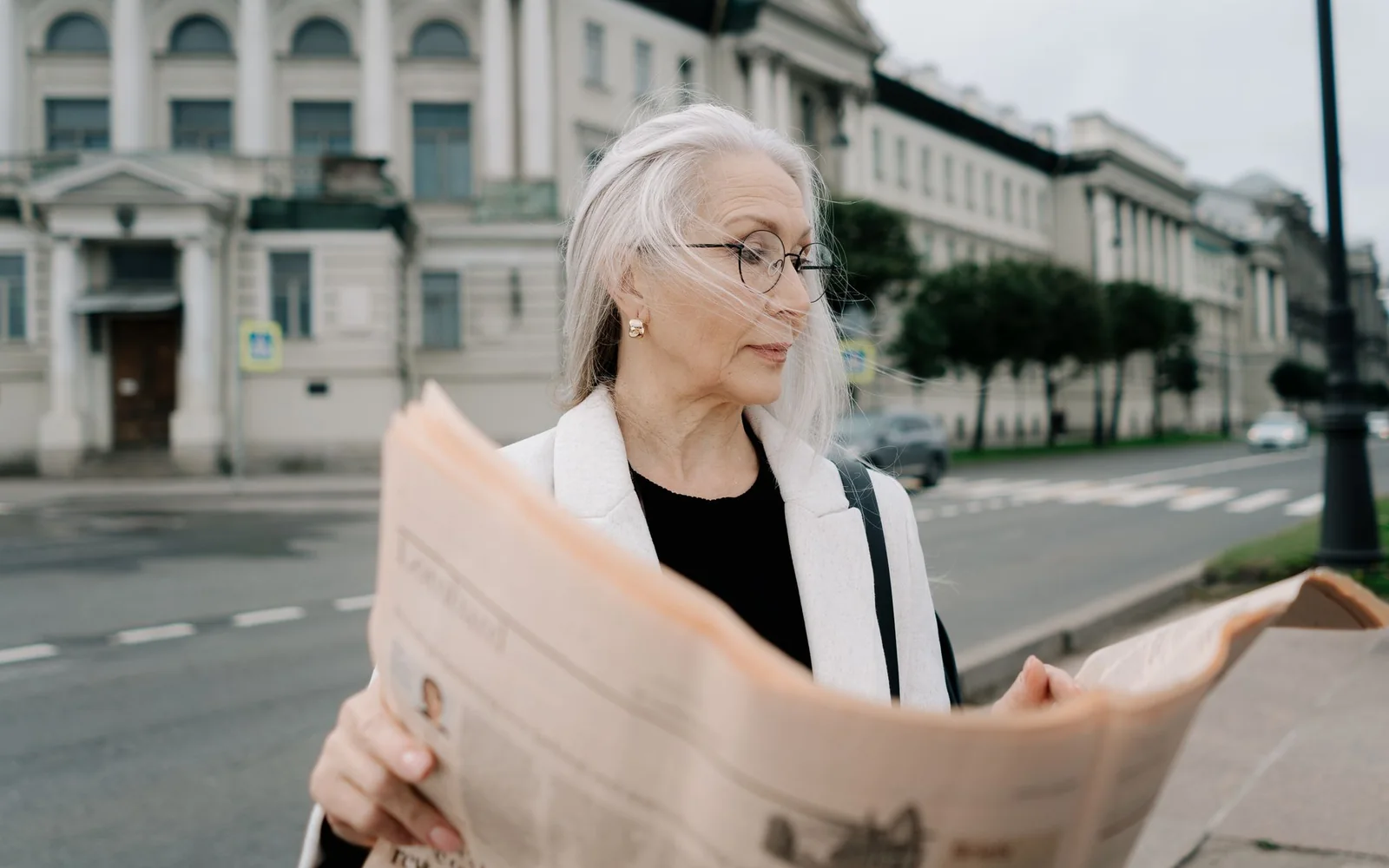 Persoană care citește purtând ochelari într-un cadru urban
